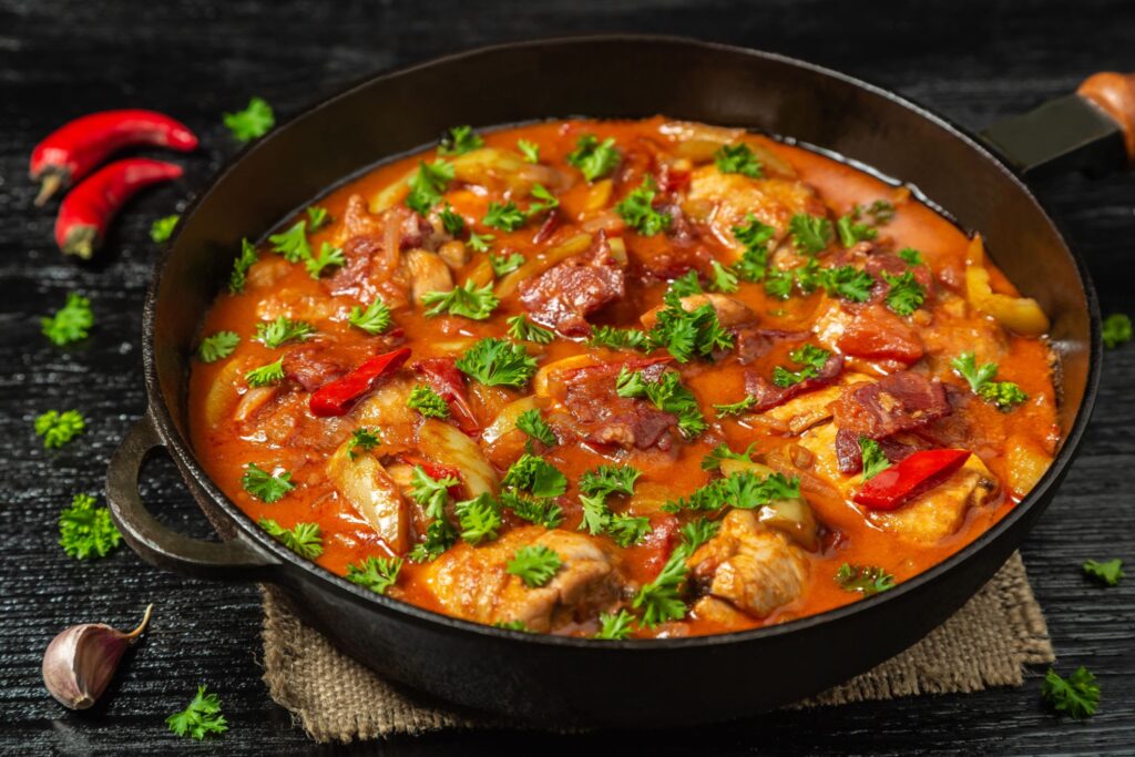 Cooking traditional Spanish chicken stew with red bell peppers and tomatoes in a pan, showcasing how to make authentic receta pollo al chilindron.
