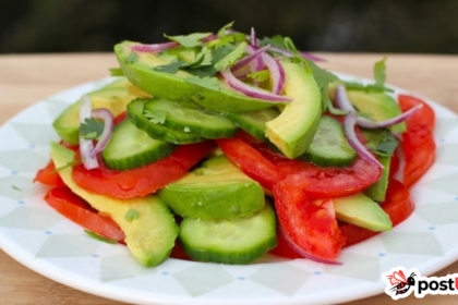 A close-up shot of a fresh Colombian salad served on a white plate with a geometric pattern. The salad is neatly arranged with vibrant layers of sliced ripe tomatoes, crisp cucumber rounds, creamy avocado wedges, and thin slivers of red onion, all topped with freshly chopped cilantro.